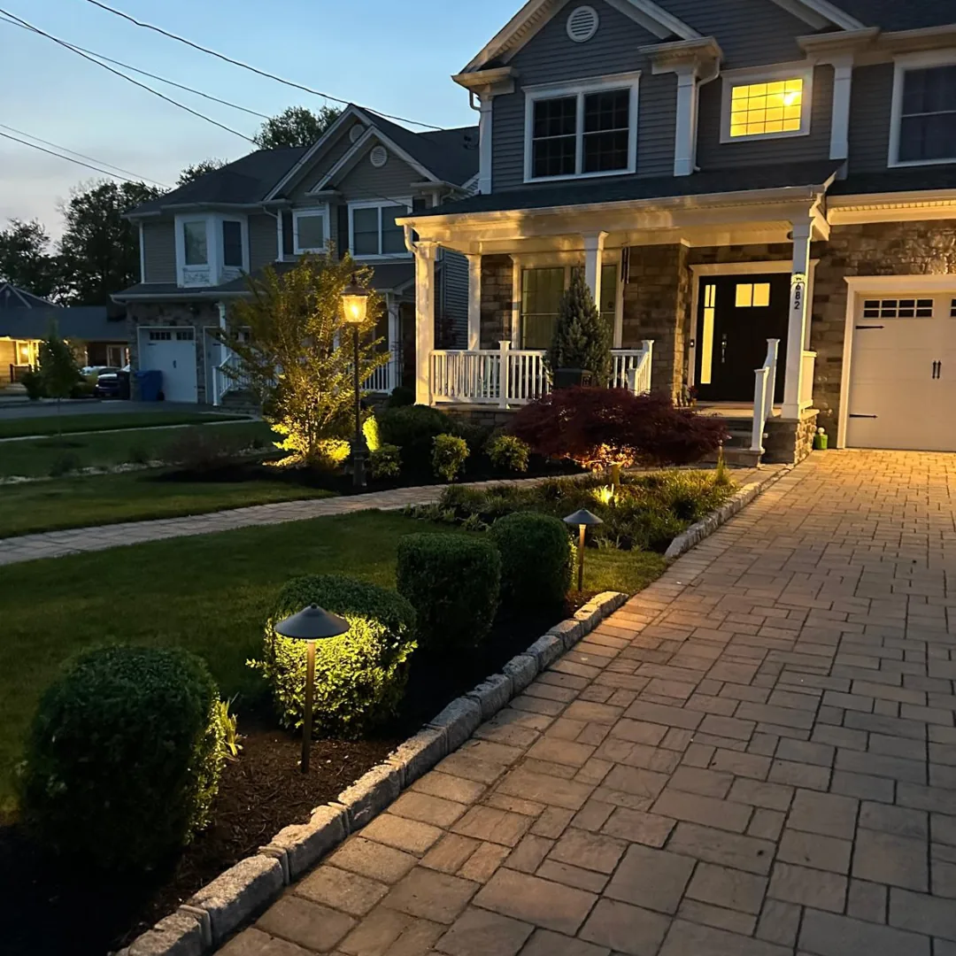 Beautifully lit front yard and paver driveway at dusk.