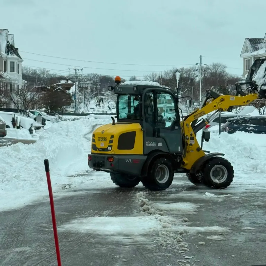 Yellow snow plow clearing snow from a parking lot.