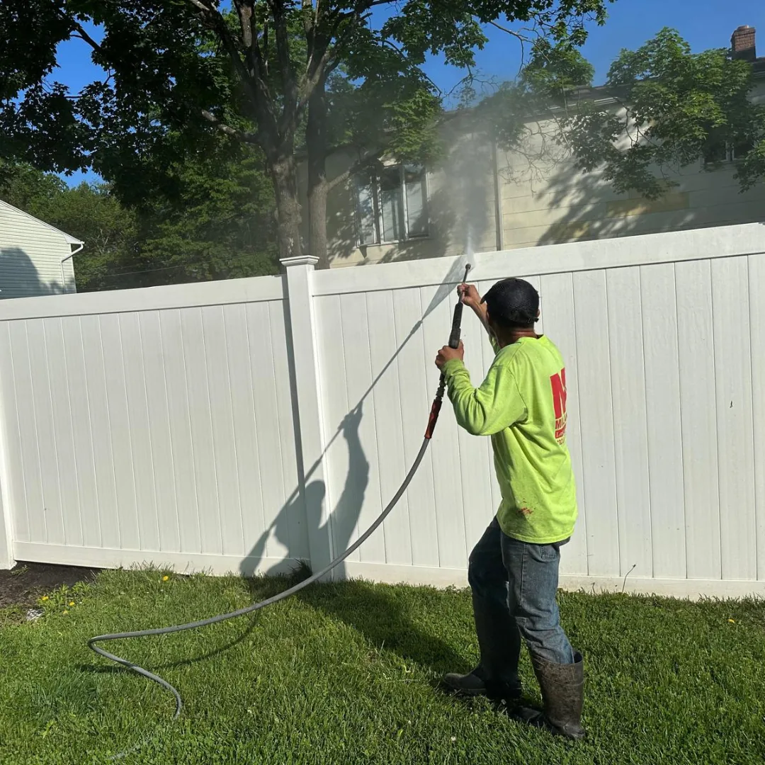 Worker power washing a white fence