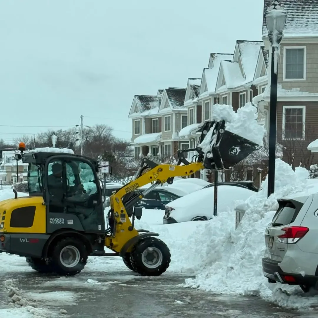 Yellow loader clearing snow from residential street.